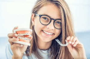 young woman with glasses and straight teeth holding invisalign aligners and 3D model of teeth with braces orthodontic treatment dentists in Bellmead Texas
